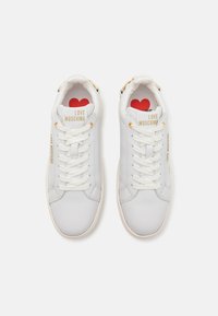 Biele kožené tenisky so zlatými akcentmi, s okrúhlou špičkou, bielymi šnúrkami a brandingom "LOVE MOSCHINO". Červený potlač srdca na vnútornej sole.