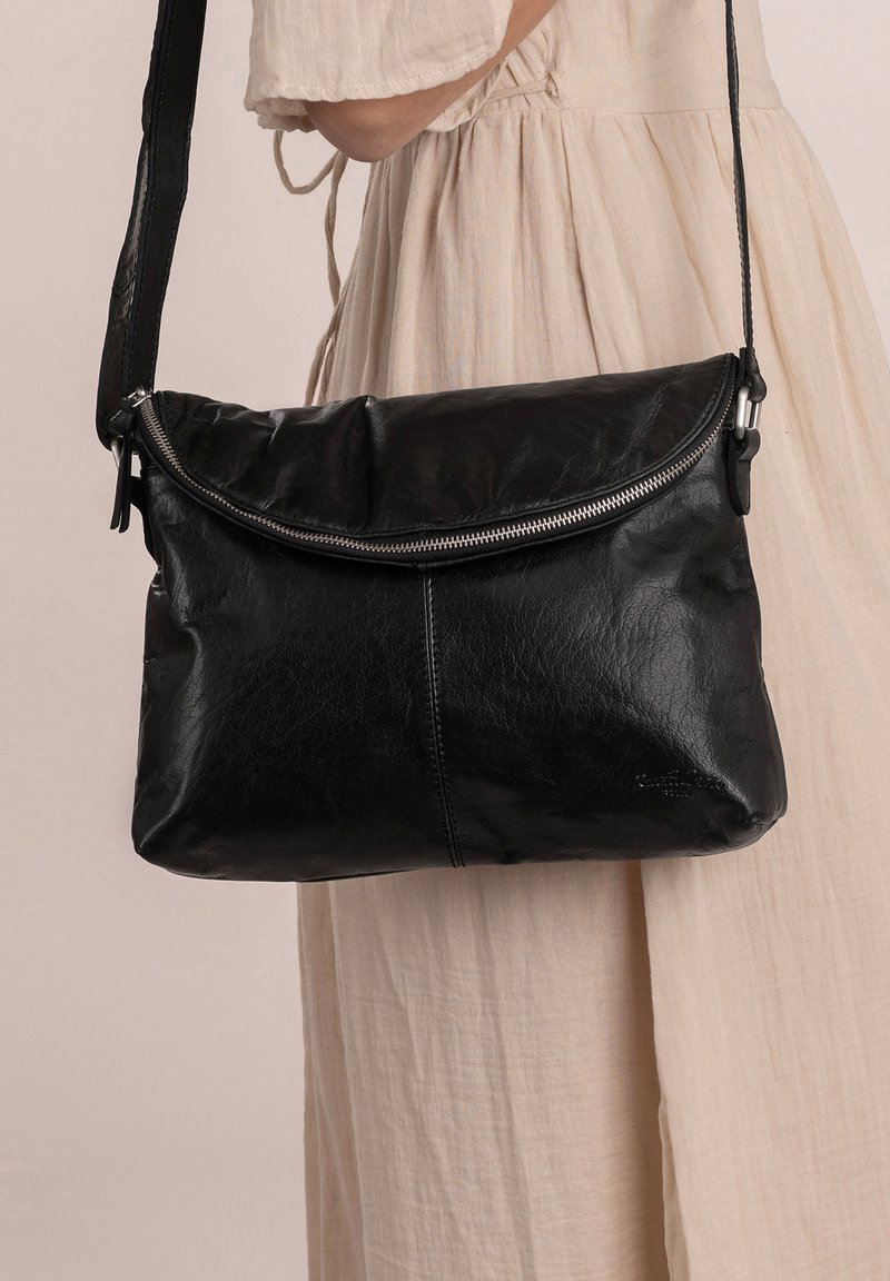 Bolso de hombro de cuero negro con cierre de cremallera, textura suave y forma redondeada. Presenta una correa desmontable y detalles de costura sutiles.