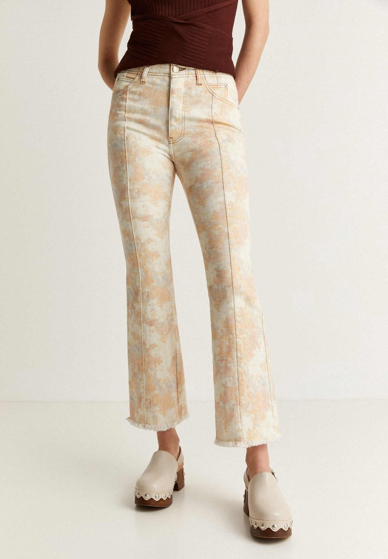 Vaqueros acampanados en colores pasteles claros con un diseño de tie-dye y dobladillos desgastados, combinados con zuecos beige con acentos decorativos.