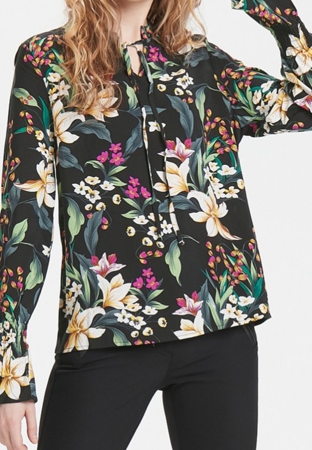Svart blus med långa ärmar och blommönster i vitt, rosa och grönt; har en knytkrage och lätt samlade ärmar.