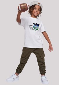White t-shirt with graphic print depicting a figure and text, paired with olive green cargo pants and white sneakers with accents.