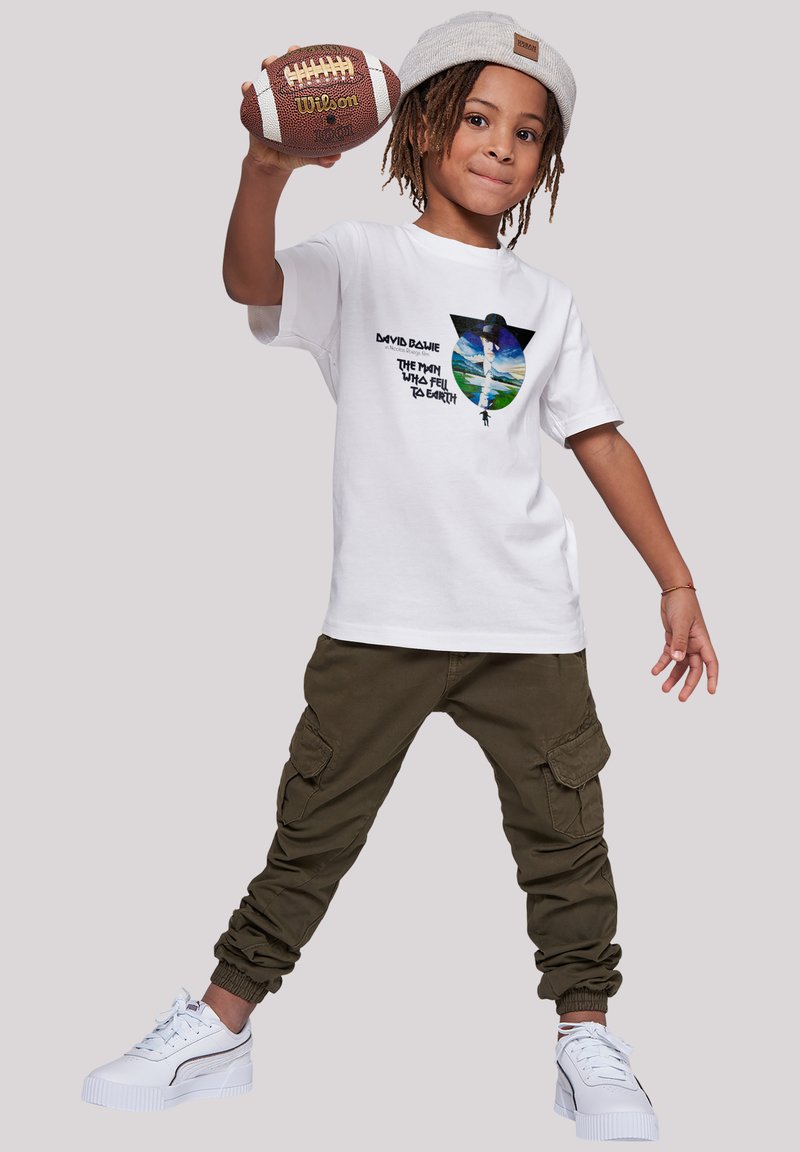 White t-shirt with graphic print depicting a figure and text, paired with olive green cargo pants and white sneakers with accents.