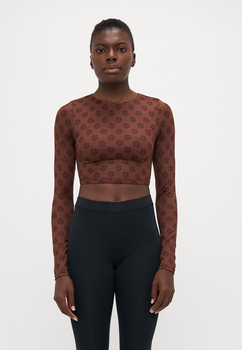 Brun blomsterlangermet croptop laget av elastisk stoff, sammen med høyt liv svarte leggings med en glatt tekstur.