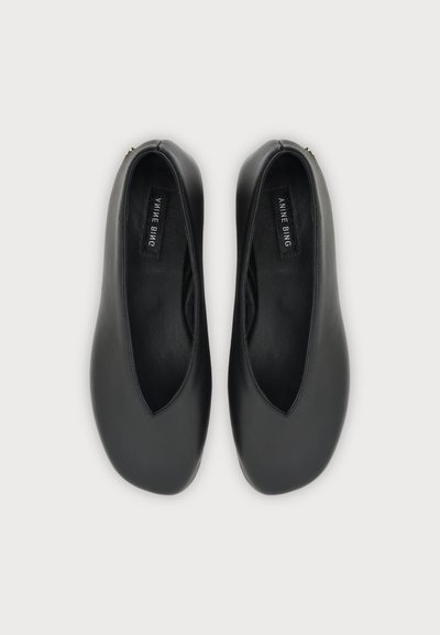 Paire de chaussures plates en cuir noir avec bouts carrés arrondis, étiquette de marque visible à l’intérieur, vue de dessus sur un fond clair uni.