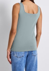 Vaaleansininen säilykepaita, jossa on neliömainen pääntie, pehmeä puuvillamateriaali, sovitettu muoto ja säädettävät olkaimet, yhdistettynä vaaleansinisiin farkkuihin.