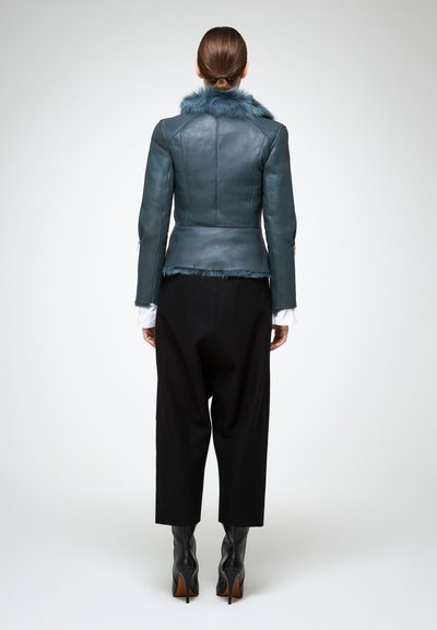 Giubbotto di pelle blu con colletto in pelliccia sintetica, vestibilità sartoriale e orlo accorciato, abbinato a pantaloni neri larghi e stivali neri con tacco alto.