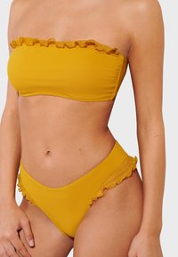 Yellow bikini with a strapless bandeau top featuring ruffled edges and matching high-waisted bottom, both in a smooth, stretchy fabric.