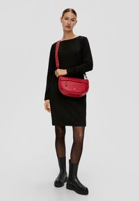 Czerwona skórzana torba na ramię o zaokrąglonym kształcie i regulowanym pasku, wyposażona w kieszeń na zamek i gładką teksturę.