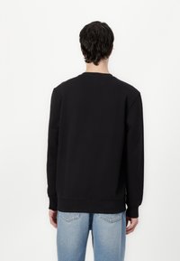 Felpa nera con maniche lunghe e collo tondo, realizzata in un tessuto spesso e liscio. Abbinata a jeans azzurri chiari che mostrano una vestibilità rilassata.