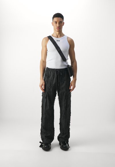 Pantalons cargo noirs texturés avec des accents effilochés, associés à un débardeur blanc ajusté. L'accessoire comprend un petit sac à bandoulière noir.