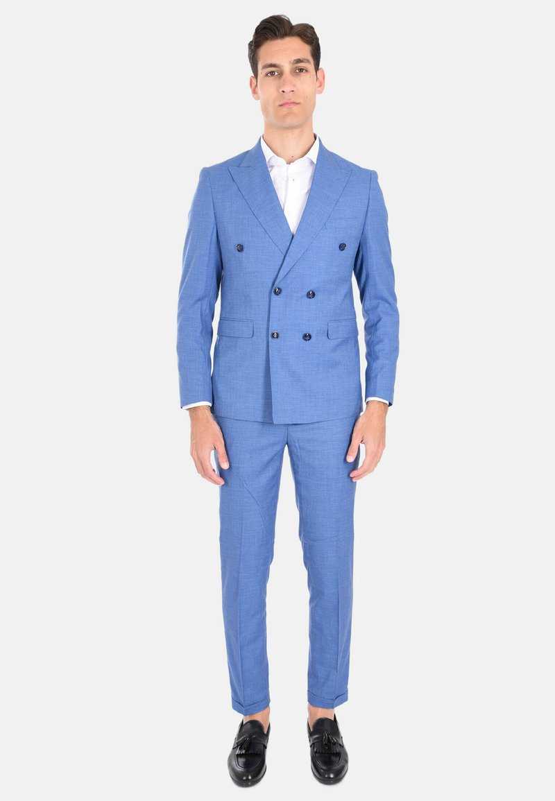 Completo azzurro chiaro a doppio petto in tessuto texturizzato, design slim fit, con bottoni scuri, abbinato a una camicia bianca e mocassini neri.