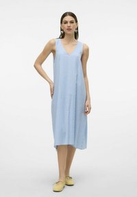 Plava i bijela prugasta haljina bez rukava s dubokim V-izrezom, lepršavog kroja i bočnim prorezima, u kombinaciji sa žutim cipelama.