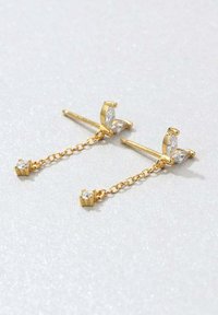 Złote kolczyki z motylkowymi wkrętami, ozdobione przezroczystymi kamieniami w szlifie markizowym; łańcuszki z małymi, osadzonymi w szprychach cyrkoniami zwisającymi poniżej.