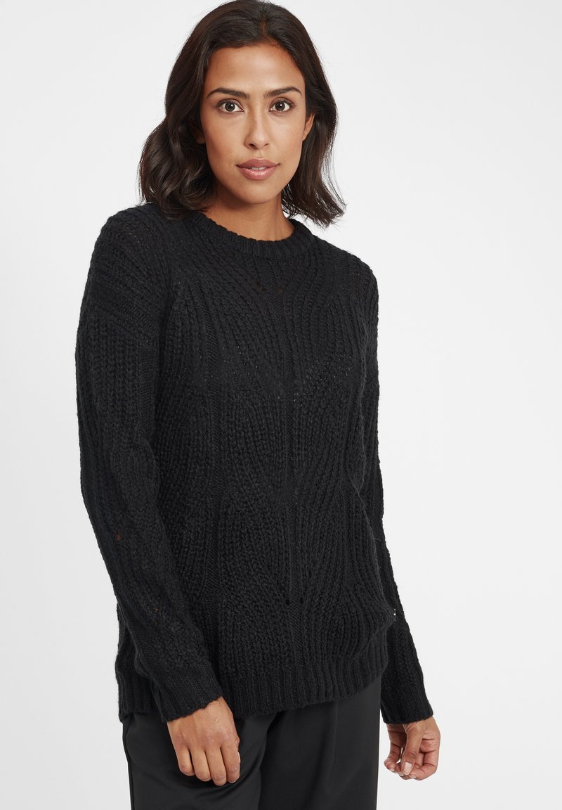 Maglione nero a maglia con un design a trecce testurizzato, scollatura rotonda e polsini e orlo a coste. Il tessuto appare spesso e accogliente.