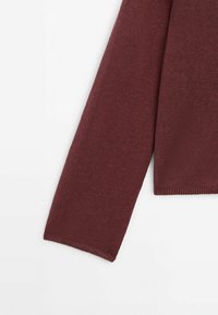 Tummanpunainen neulehihna, neulottu pinta, istuva muotoilu siistillä reunuksella. Hiukan resorimainen hihansuussa, korostaen rikasta, syvää väriä.