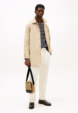 Beige lett jakke med knap closures, stripet marineblå og hvit skjorte, kremfargede bukser og svarte loafers. Holder en lys og marineblå crossover-veske.