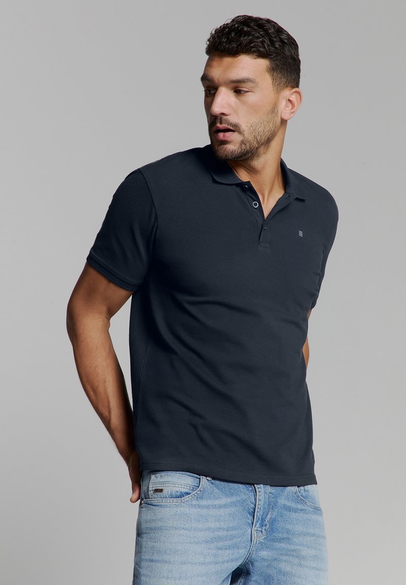 Marineblauwe polo shirt van een gladde katoenmix, met een kraag met twee knopen en een klein logo op de borst, gecombineerd met lichtblauwe jeans.