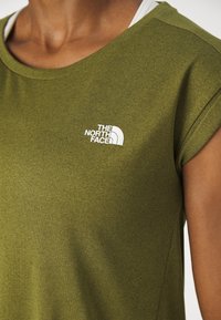 Olivgrön t-shirt med kort ärm, tillverkad av mjukt tyg, med en vit logotyp av "The North Face" på bröstet.