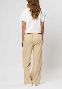 Beige, brede bukser lavet af blødt materiale med elastisk talje. Sæt sammen med en hvid skjorte med korte ærmer. Hvide sneakers synlige.