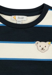 Camicia di cotone a righe navy e crema con un patch ricamato a forma di faccia d'orso con un accento giallo. Collo rotondo con finitura a coste.
