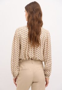 Blusa beige chiaro con stampa floreale in rosa e verde. Maniche lunghe con polsini arricciati e vestibilità leggermente rilassata all'orlo.