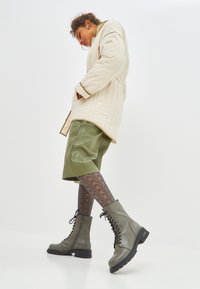 Beige gewatteerde jas, groene nep leren shorts, patroon panty's en groene veterboots met een stevige zool. Schoon, modern ontwerp.