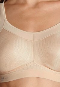 Beige sports bra with textured mesh panels. Smooth edges and structured design for support. Logo on the band at the bottom.