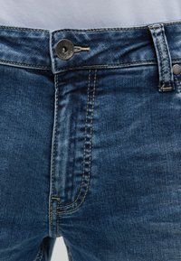 Blaue Denim-Jeans mit einem Frontknopfverschluss, kontrastierenden Nähten und einer zerschlissenen Textur. Verfügt über einen geraden Schnitt und traditionelle Taschen.
