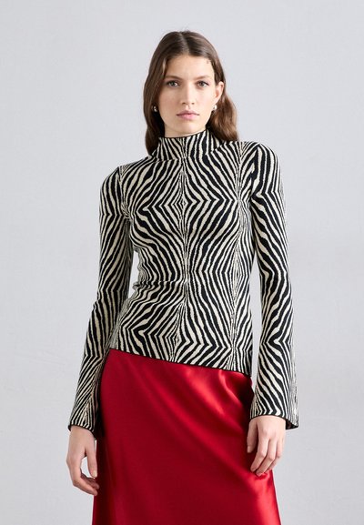 Haut à col montant rayé noir et blanc avec des manches longues et une silhouette ajustée, associé à une jupe en satin rouge lisse.