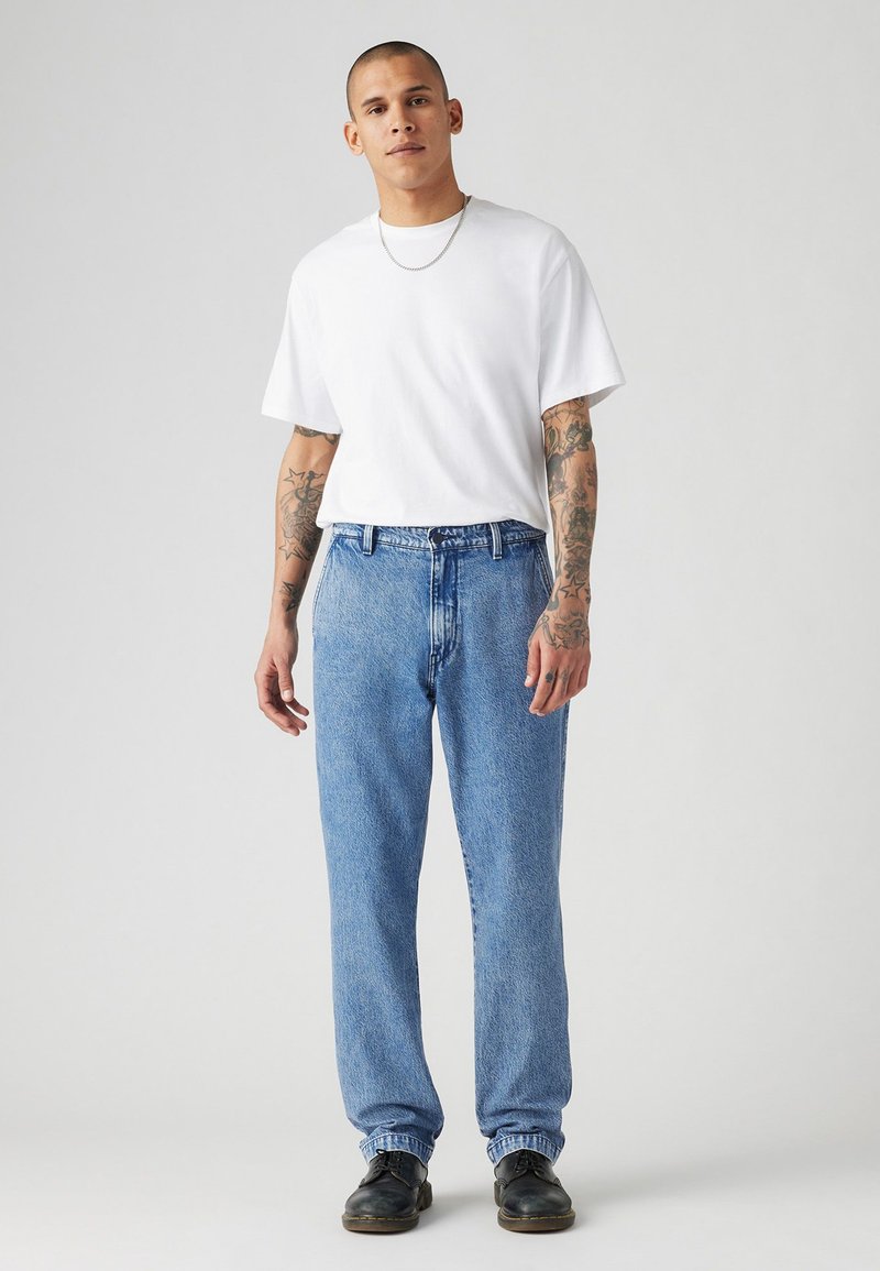 Weißes T-Shirt mit kurzen Ärmeln, kombiniert mit hellblauen, leicht verwaschenen Damenjeans im geraden Schnitt, abgerundet mit schwarzen Schuhen. Einfaches Design und lockere Passform.