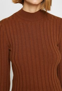 Brązowy sweter z prążkowanej dzianiny z wysokim dekoltem i długimi rękawami, prezentujący pionowe paski i miękką teksturę.