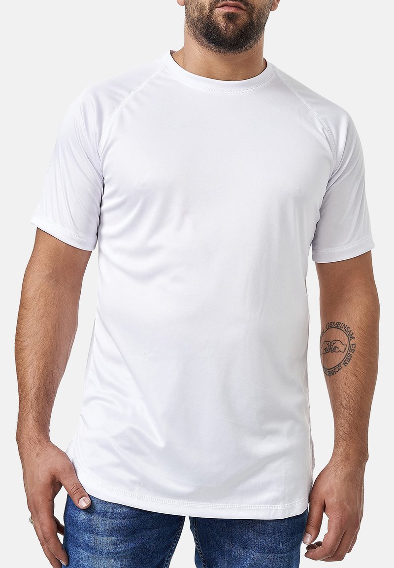 Camiseta atlética de manga corta blanca, hecha de tejido que absorbe la humedad, con cuello redondo y textura suave, usada con jeans azules.