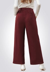 Wijd uitgesneden broek in bordeauxrode stof, met een gladde textuur, hoge taille en subtiele plooien. Gepaard met witte hoge laarzen.