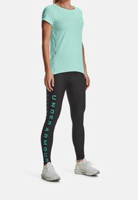 Jasnozielona koszulka z krótkim rękawem w zestawieniu z czarnymi legginsami z pionowym nadrukiem w kolorze aqua. Modelka ma na sobie lekkie buty sportowe.