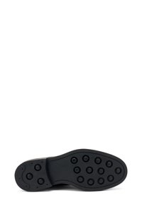 Suola di scarpa in gomma nera con motivi di grip circolari e bordi lisci. Progettata per aderenza e durata, piatta con una punta arrotondata.