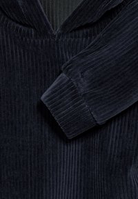 Il tessuto in corduroy blu navy presenta un motivo a coste verticali, un collo con cappuccio e una texture morbida con dettagli maniche a polsino.