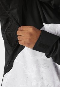 Schwarze und weiße Jacke mit strukturiertem Stoff, Netzstasche und Klettverschluss an den Bündchen, mit einem modernen Farbschema.