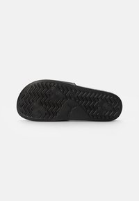 Semelle de chaussure noire avec un motif de traction texturé ; présente des designs hexagonaux et en zigzag, fabriquée en caoutchouc, avec un logo en relief au bas.