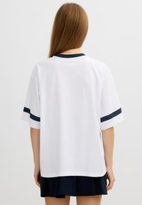 Camiseta blanca con rayas marinas en las mangas y el cuello, hecha de algodón; corte relajado con mangas cortas y un dobladillo redondeado en la parte posterior.