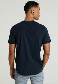 Tumesinine lühikeste varrukatega T-särk ümmarguse kaelusega, millel on kinnitus detail tagaküljel ja sirge äär. Puuvillane materjal, juhuslik lõige.