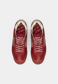 Ζευγάρι κόκκινων αθλητικών παπουτσιών της μάρκας Replay με λευκές και καφέ λεπτομέρειες, εσωτερικά πέλματα με σχέδια και ροζ κορδόνια, απεικονισμένα από πάνω σε λευκό φόντο.