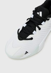 Chaussure de sport blanche avec des accents noirs, dotée d'une tige en mesh texturé, de lacets contrastés et d'un design épuré et profilé.