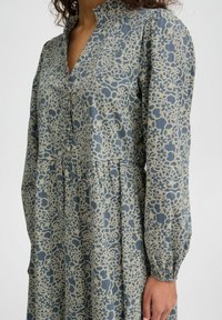 Abito blu con motivo floreale in pizzo beige, colletto rialzato, maniche lunghe, vita arricciata e tessuto testurizzato.