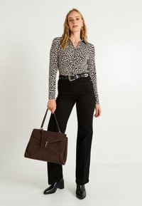 Blouse à imprimé léopard en noir et blanc, associée à un jean noir taille haute et un sac en suède marron. Des bottes à talons noires complètent le look.