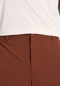 Pantaloni marroni dalla texture liscia, con vita a metà altezza, chiusura a un solo bottone e dettagli di cucitura sottili lungo le cuciture.