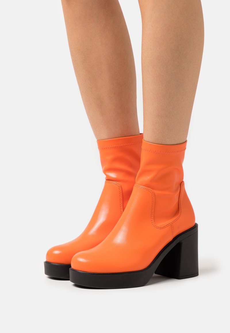 Botas de tobillo de cuero naranja con un acabado suave, que cuentan con un tacón grueso negro y tejido elástico en la parte superior para un ajuste ceñido.