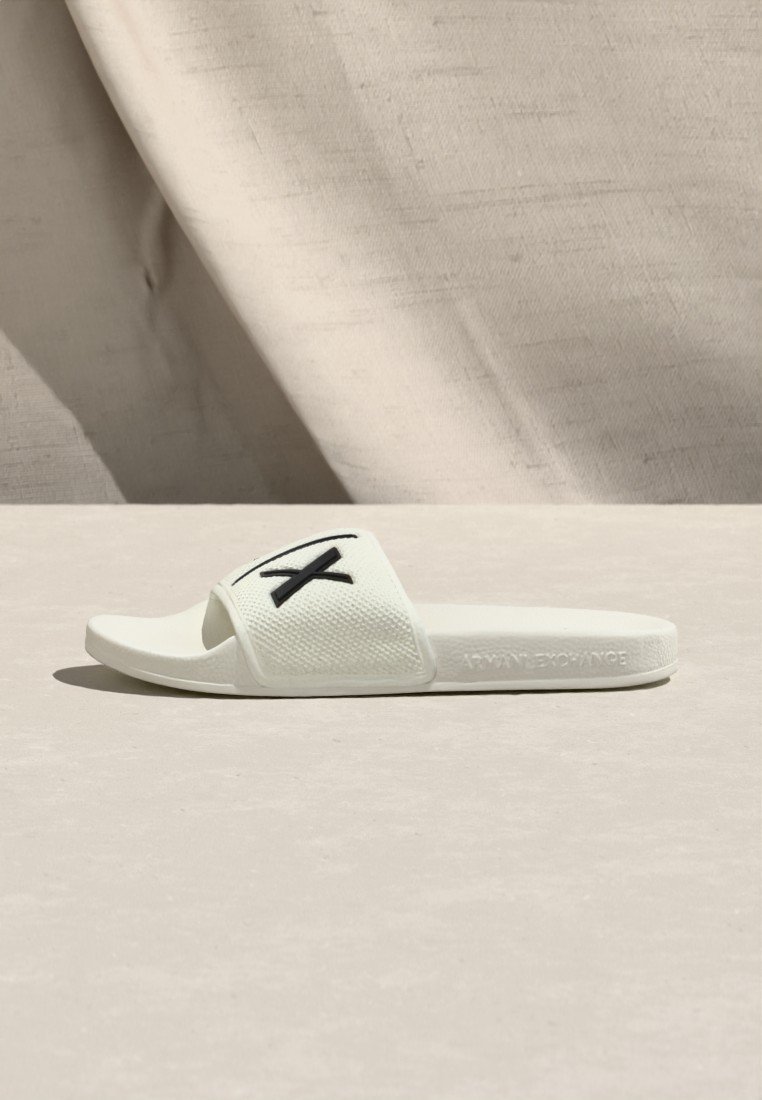 Sandale à glissière blanche avec une bride texturée ornée d'un motif de croix noire, une semelle intérieure lisse et "ARMANI EXCHANGE" embossé sur la semelle.