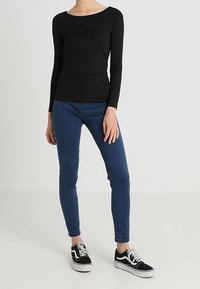 Svart långärmad topp med rund halsringning, kombinerad med blå skinny jeans och svarta sneakers. Outfitten har en figurnära silhuett.