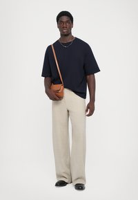 Ναυτικό oversized T-shirt, μπεζ παντελόνι με φαρδιά πόδια, μαύρα παπούτσια και καφέ τσάντα ώμου με λουρί, σε λευκό φόντο.