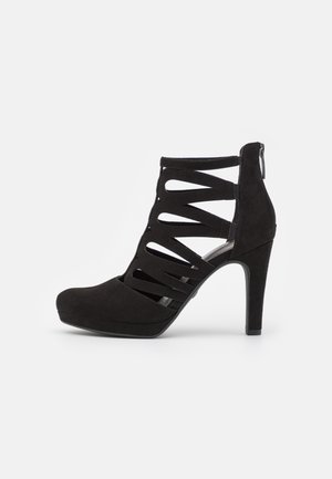 Zwarte suède high-heel enkelboots met uitsnijdingen, ronde neus en achterrits. Voorzien van een plateau voor extra hoogte.